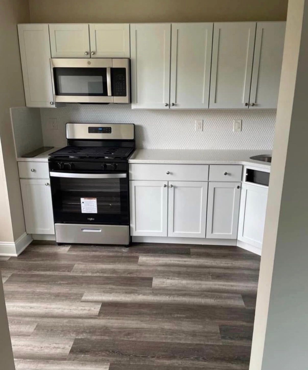 Small modern kitchen with white cabinets, stainless steel appliances, and gray wood-look flooring.