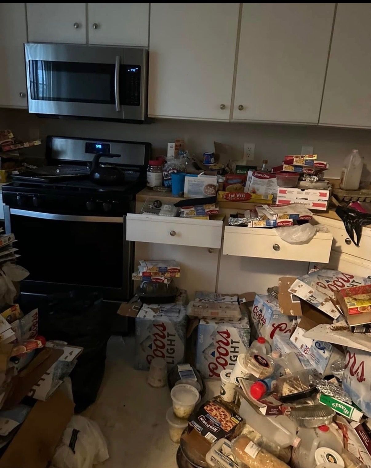 Cluttered kitchen with open drawers and cabinets, boxes and groceries scattered on the counters and floor.