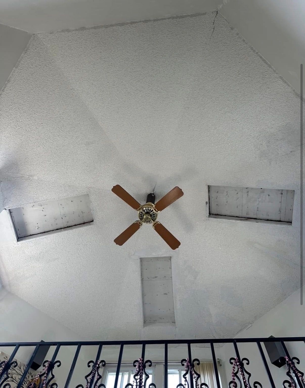 White ceiling with a brown ceiling fan and three rectangular skylights over a dark railing.