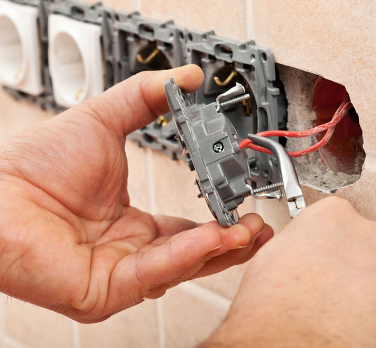 Hand holding a wall outlet switch with exposed red wires during electrical installation