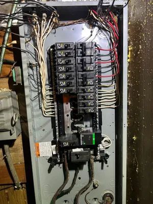 Open electrical breaker panel with many labeled switches and exposed wiring.