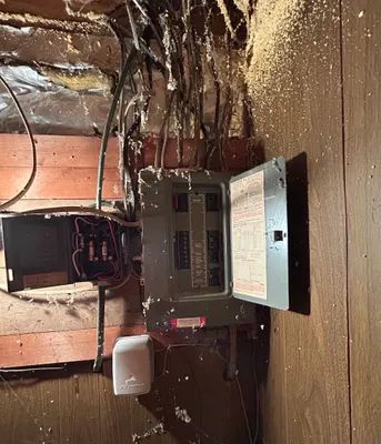 Open electrical breaker panel in a damaged wall with exposed wiring and insulation.
