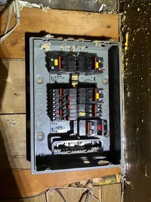Open electrical breaker panel with rows of switches mounted in a wooden wall opening.