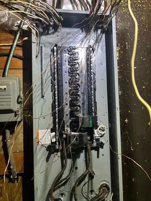 Open electrical breaker panel with exposed wires and wires hanging around it
