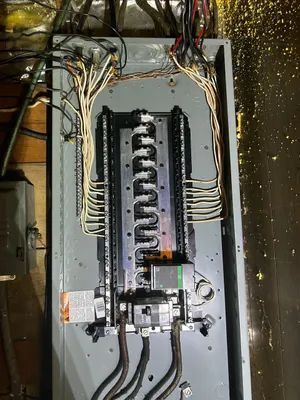 Electrical breaker panel with exposed wiring and circuits in a gray metal box inside a utility area