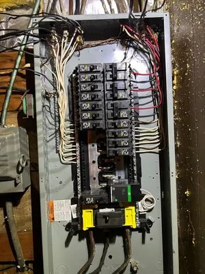 Electrical breaker panel with exposed wiring and circuit breakers in a utility space.