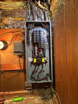 Open electrical breaker panel on wood wall with exposed wires and a yellow lockout device