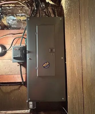 Electrical breaker panel mounted on a wood wall with exposed wiring and insulation nearby