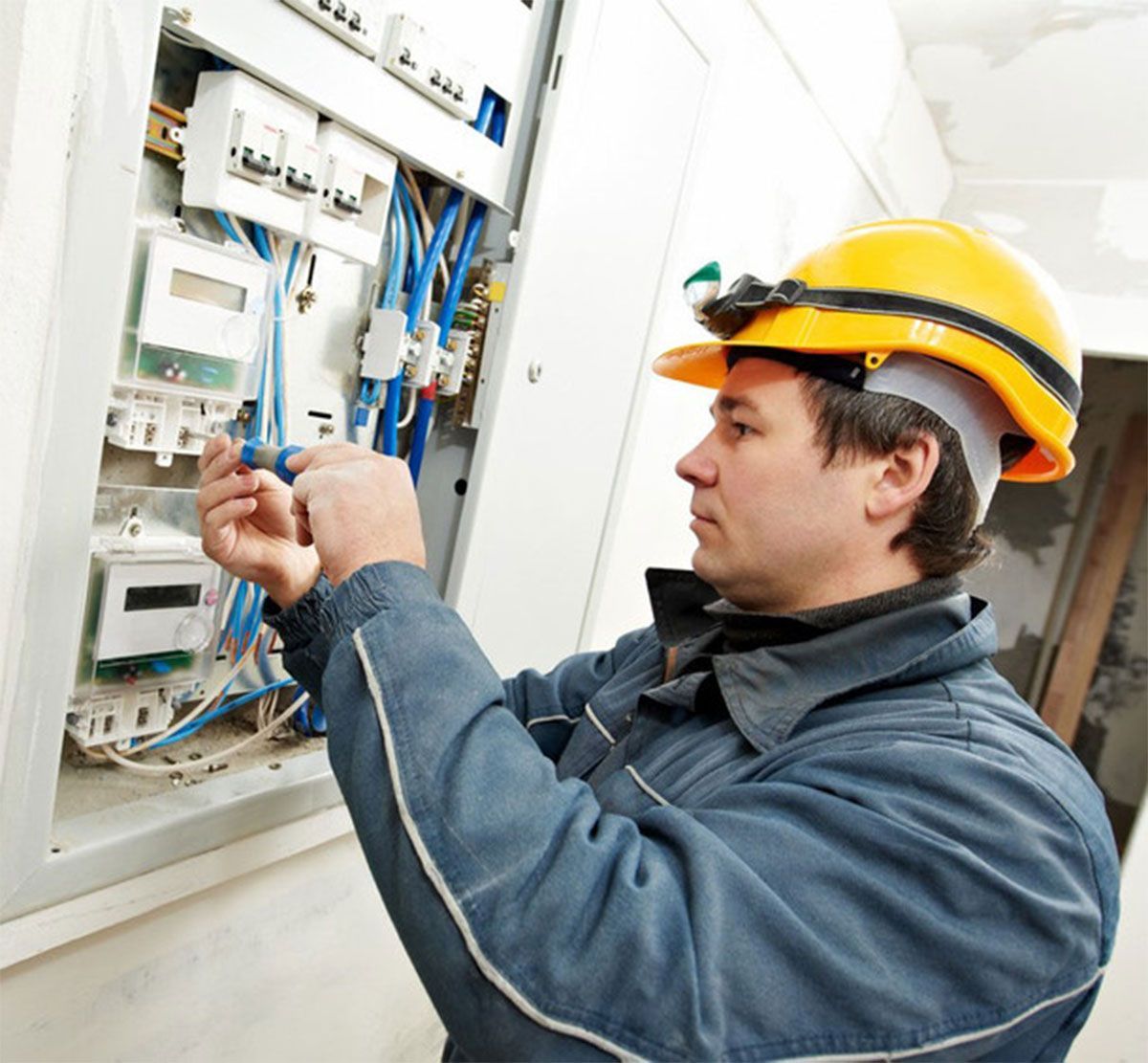 Technician in yellow hard hat wiring an electrical control panel