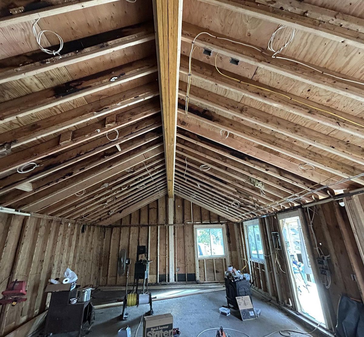 Unfinished attic with exposed wooden rafters, insulation, and construction materials scattered on the floor.