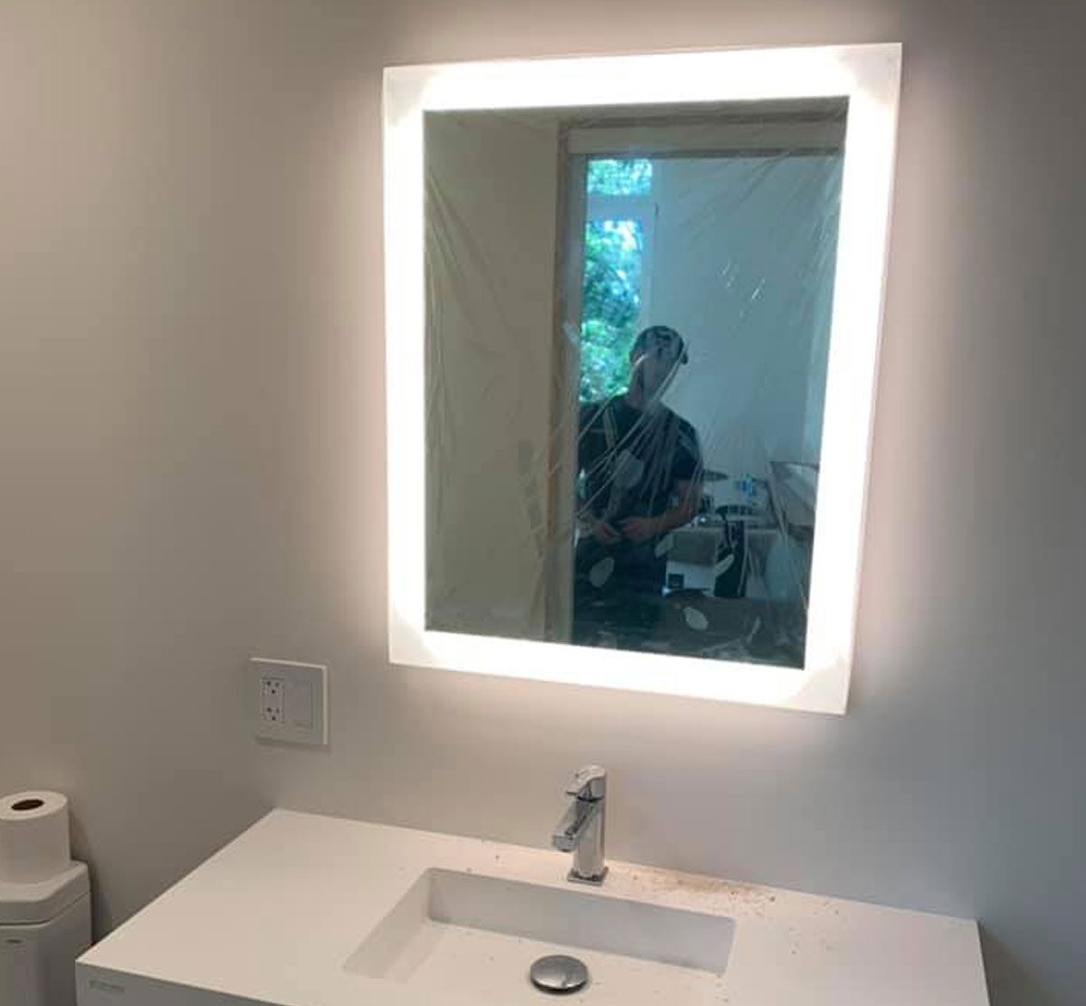Bathroom vanity with illuminated mirror reflecting a person taking the photo