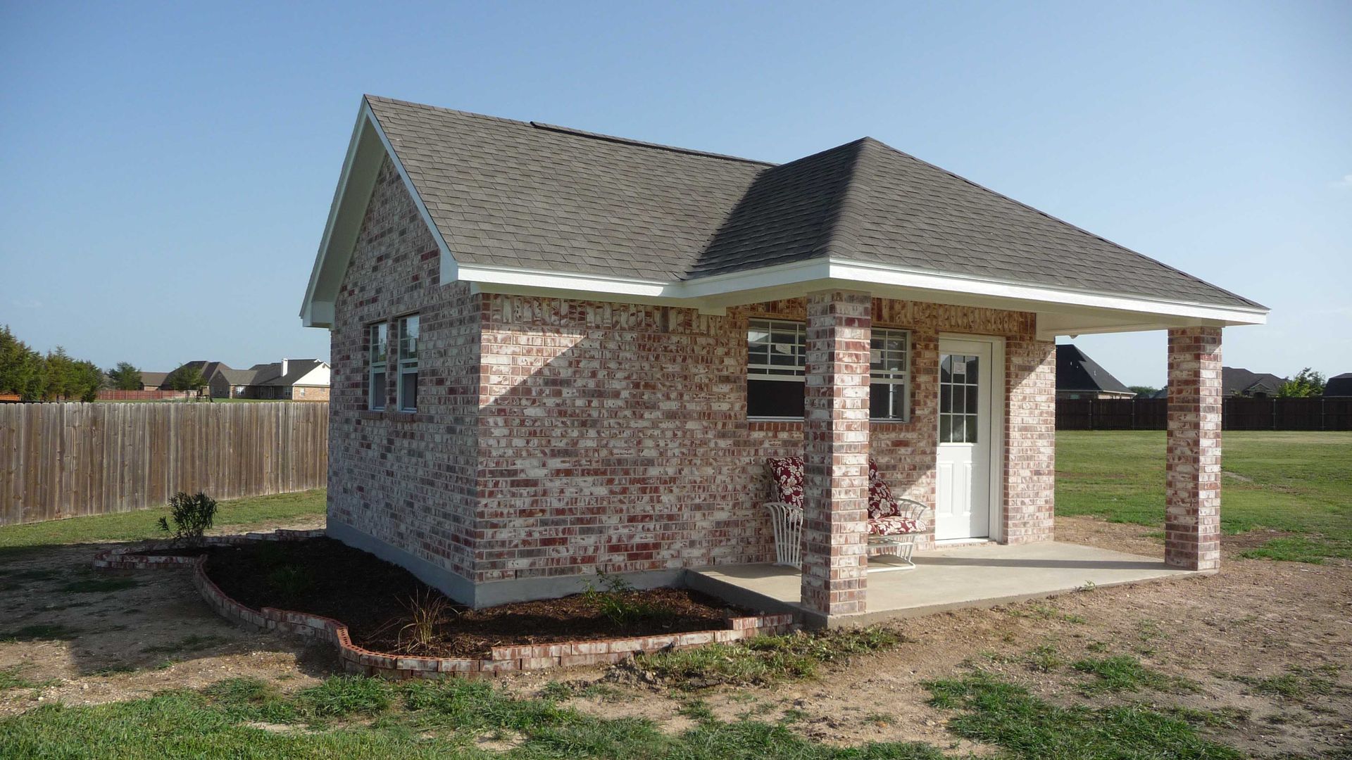 A small brick house with a porch in the backyard