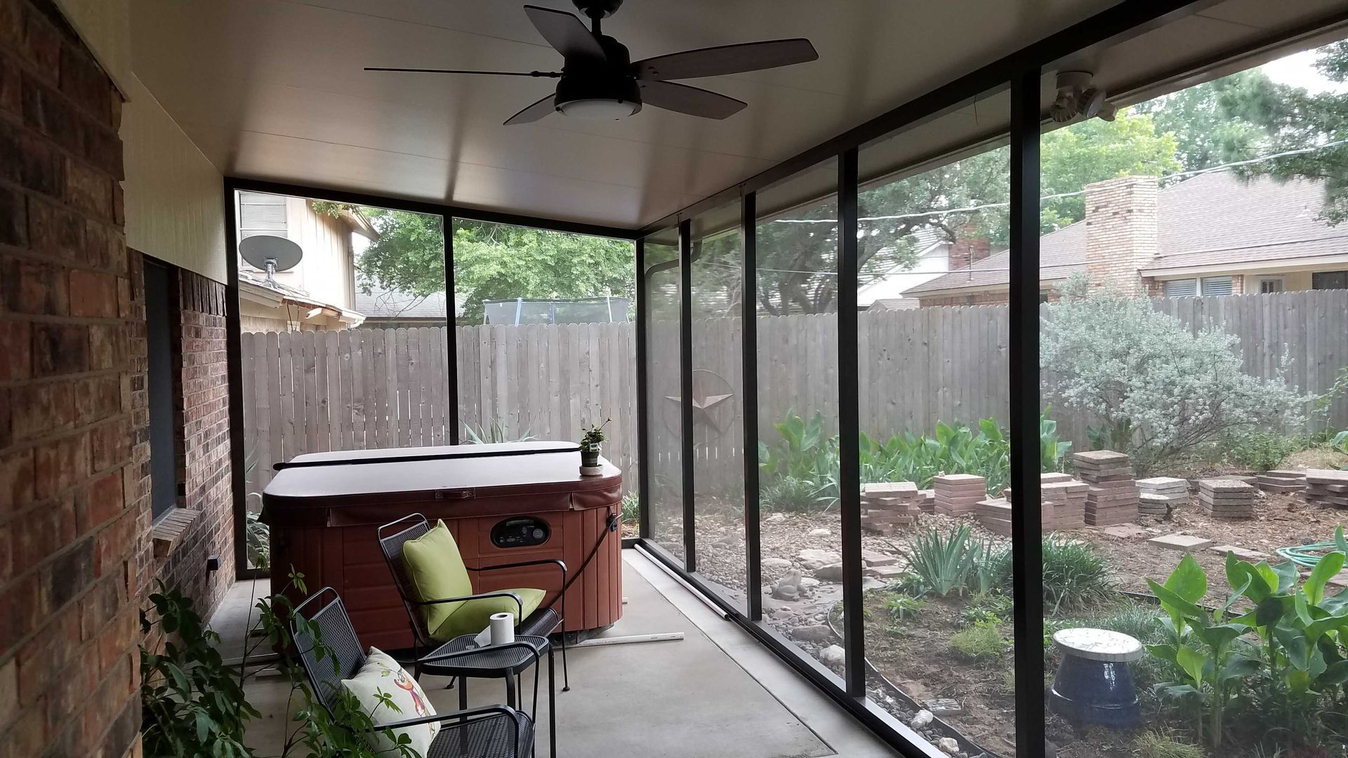 A screened in porch with a hot tub and a ceiling fan.