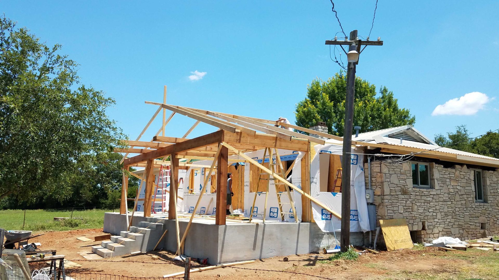 A house is being built in a field with a telephone pole in the foreground.