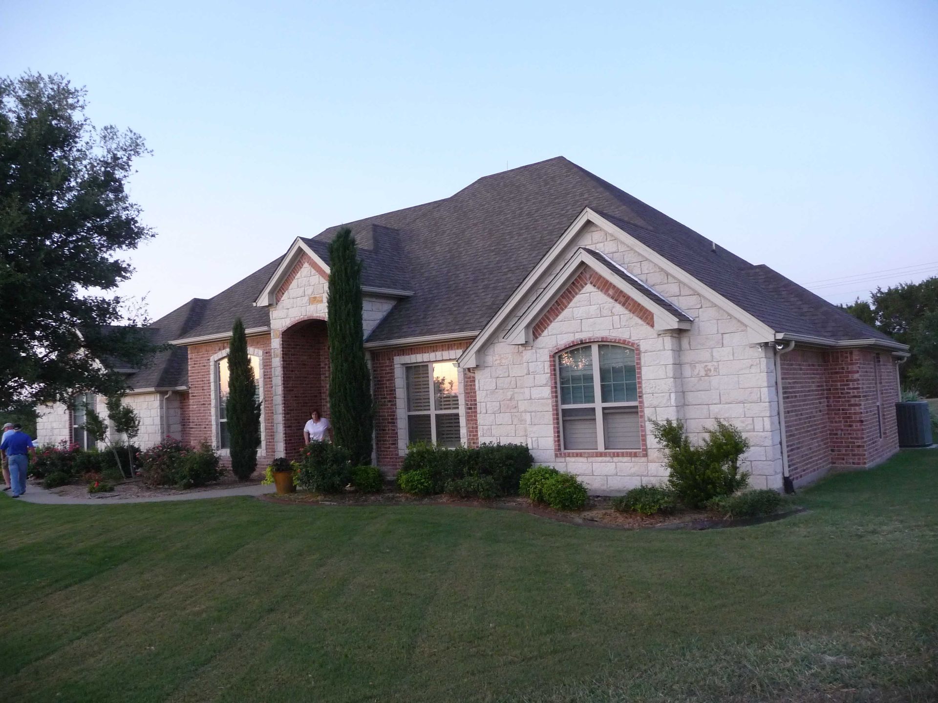 A man stands in front of a large brick house