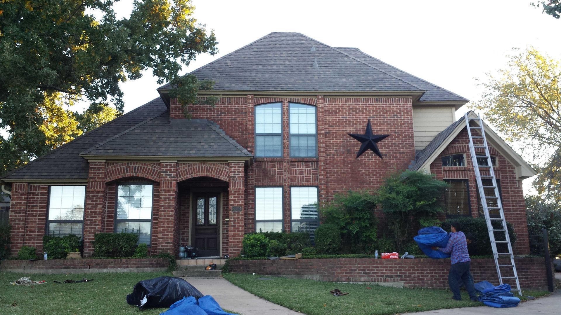 A man is standing in front of a large brick house with a star on the roof.