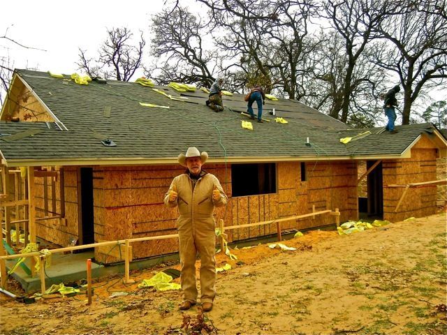 A man in a cowboy hat is standing in front of a house under construction