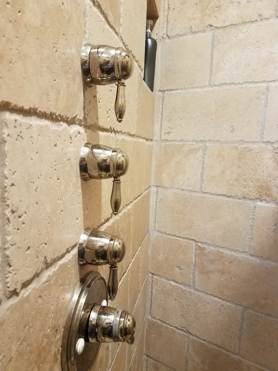A close up of a shower faucet on a tiled wall.