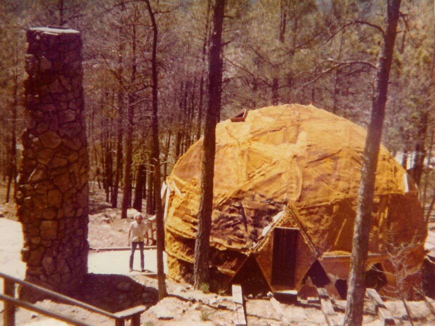 A large dome is surrounded by trees and a stone chimney