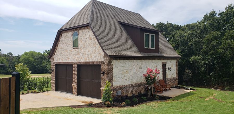 A garage with two garage doors is sitting in the middle of a lush green field.
