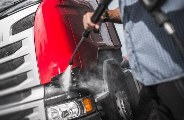 A man is cleaning a red truck with a high pressure washer.