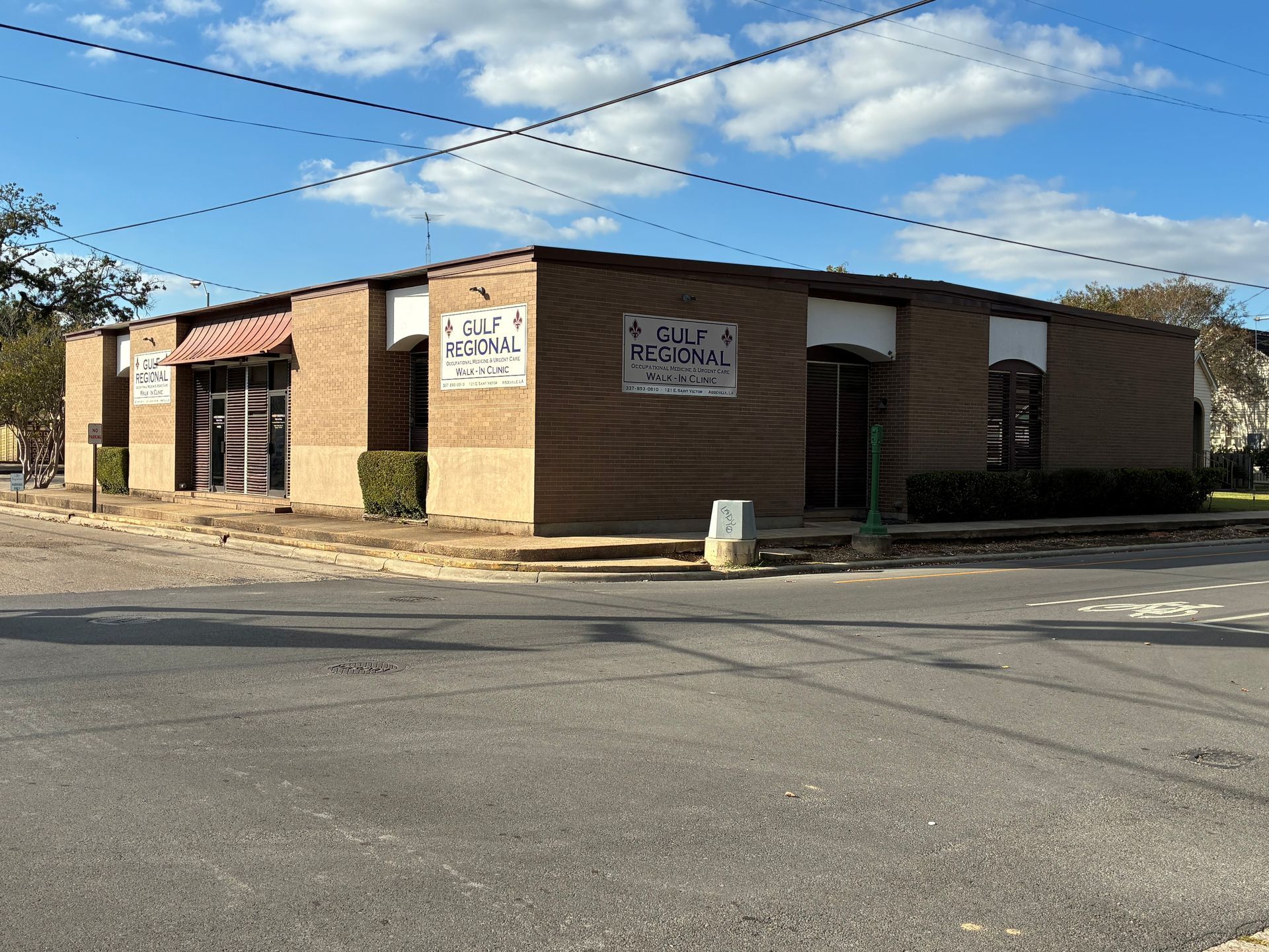 Brick building with two visible business storefronts and signs, on a street corner, with cloudy sky.