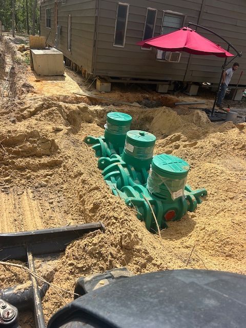 Green septic tank installation in a sandy yard, near a house with an umbrella
