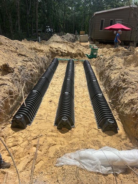 Three black septic system leach fields in a sandy trench at a construction site near a small building