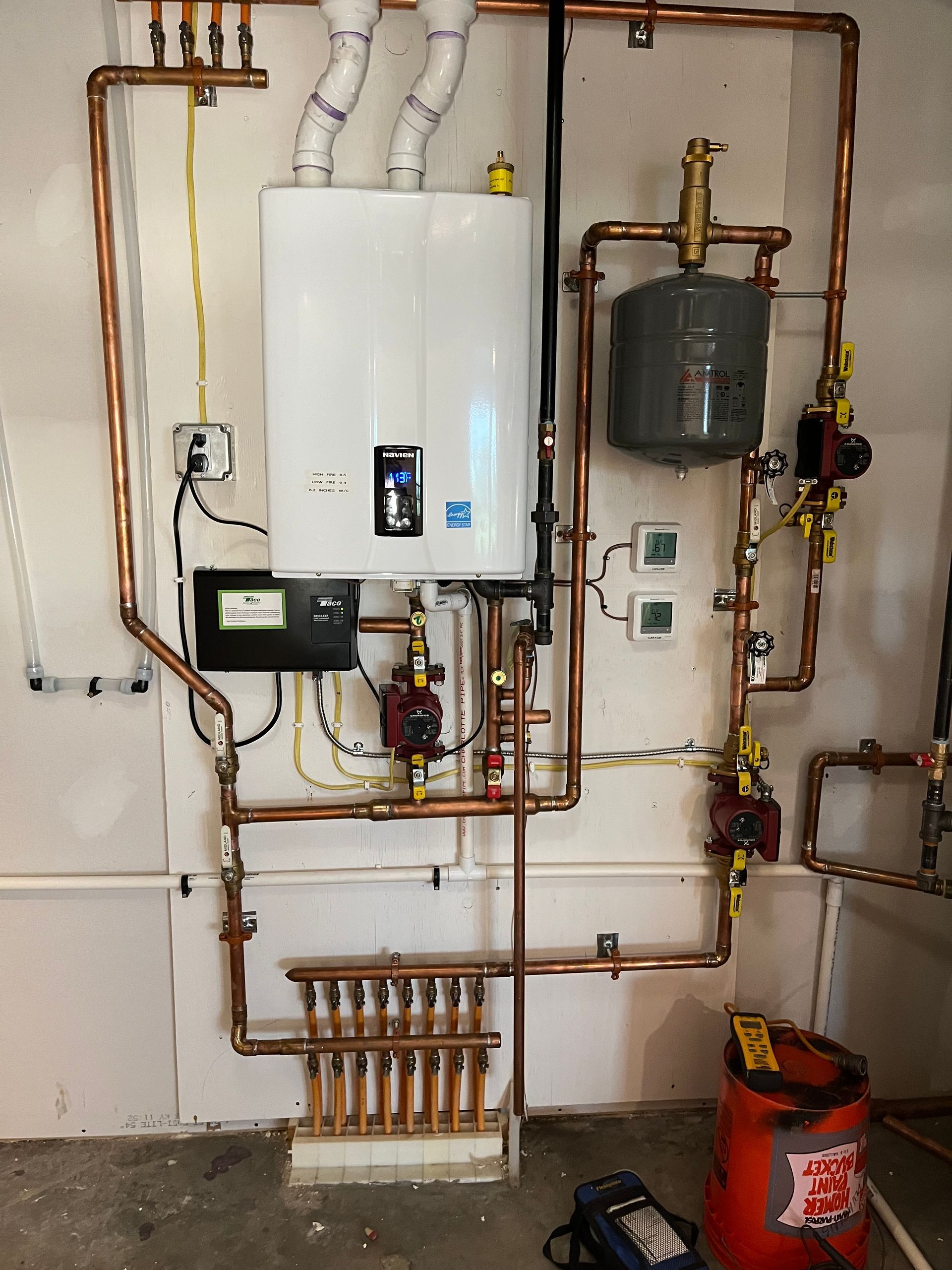 White wall-mounted water heater with copper pipes, valves, and a small expansion tank.