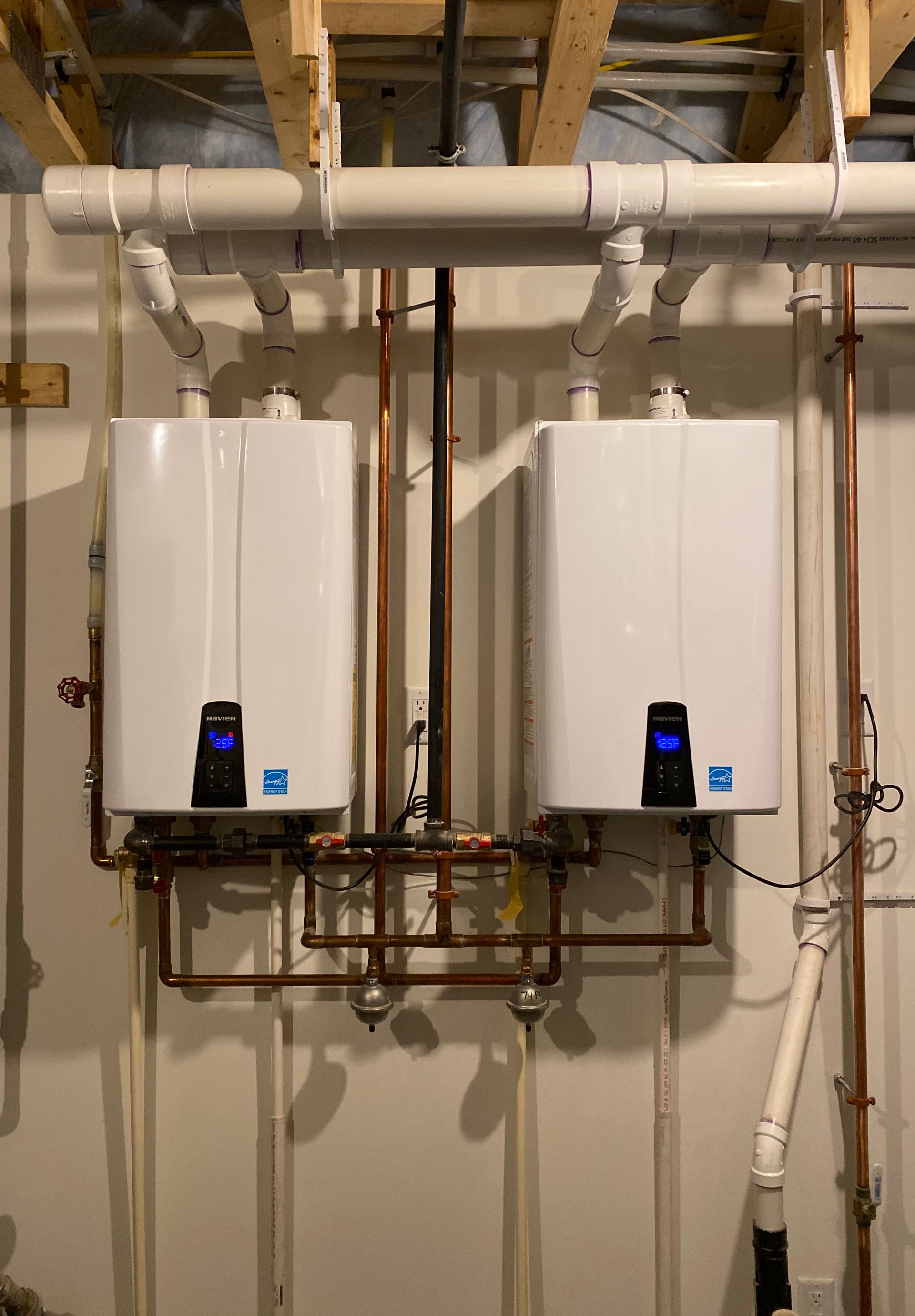 Two white tankless water heaters mounted on a wall with copper pipes.
