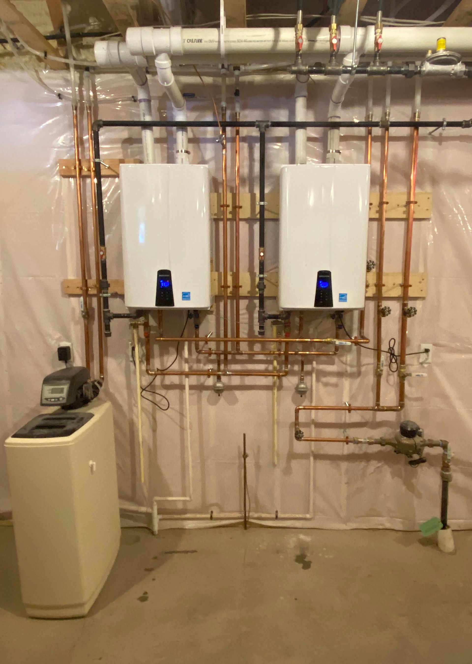 Two white water heaters and water softener with copper pipes installed against a wall.