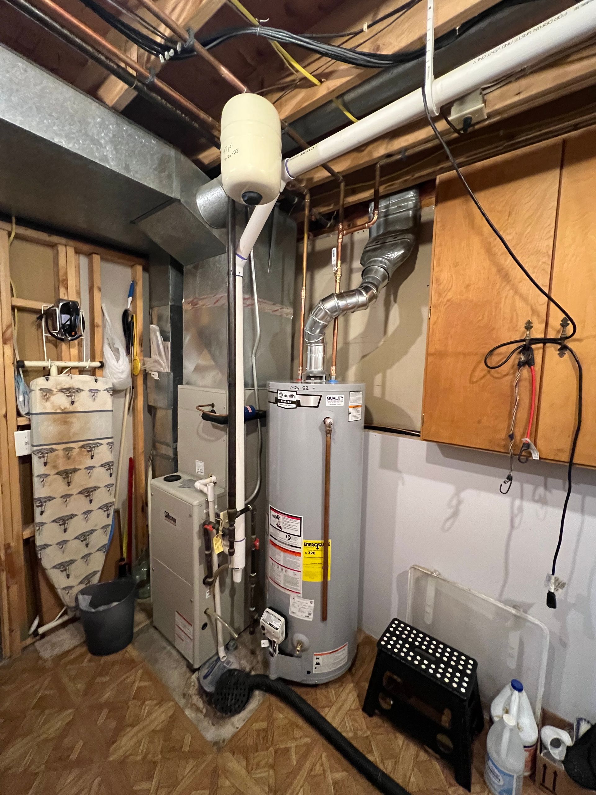 Basement with furnace, water heater, pipes, and electrical components against wood walls.