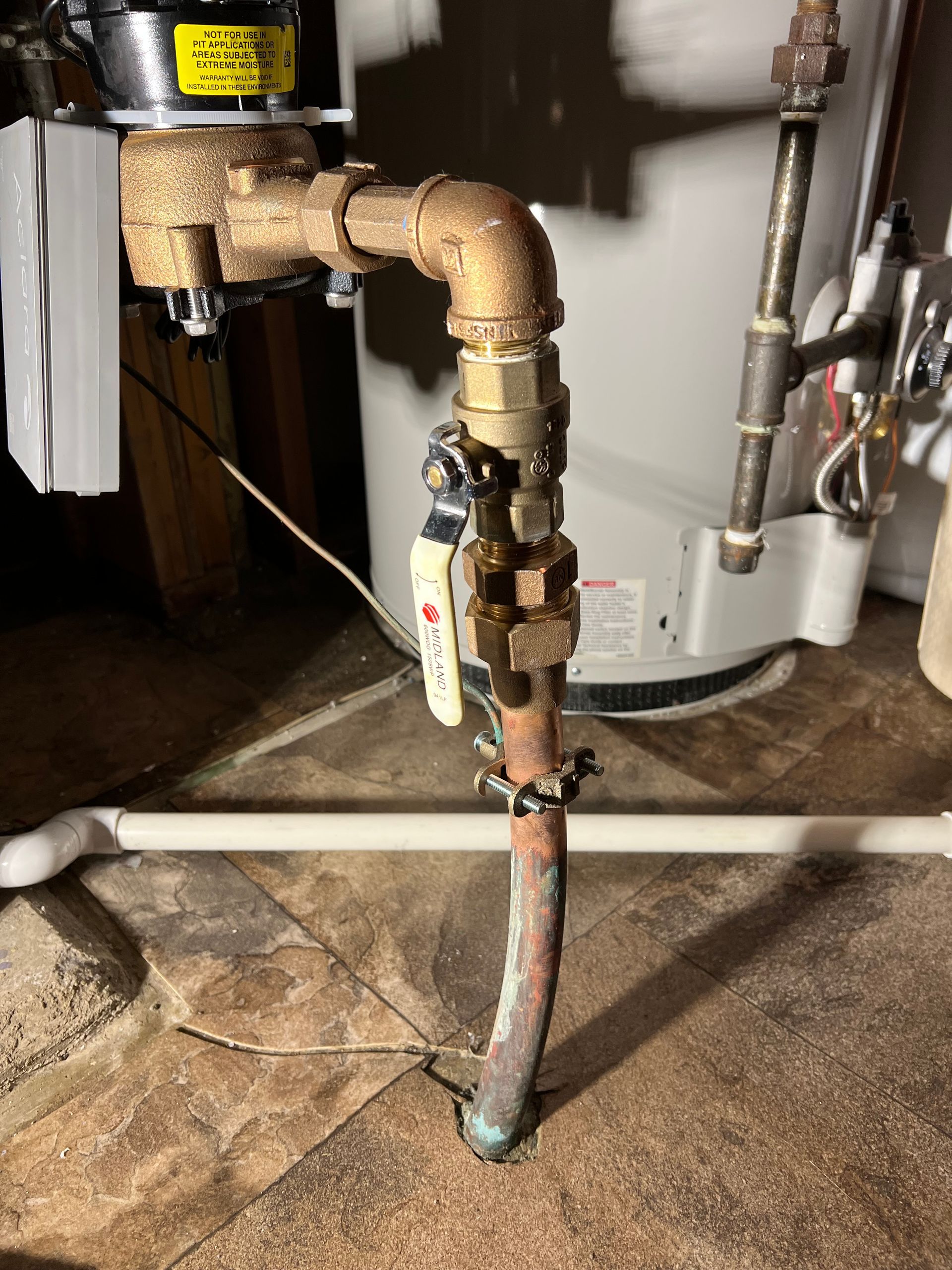 Copper pipe connected to a water heater with a valve and brass fittings in a basement.