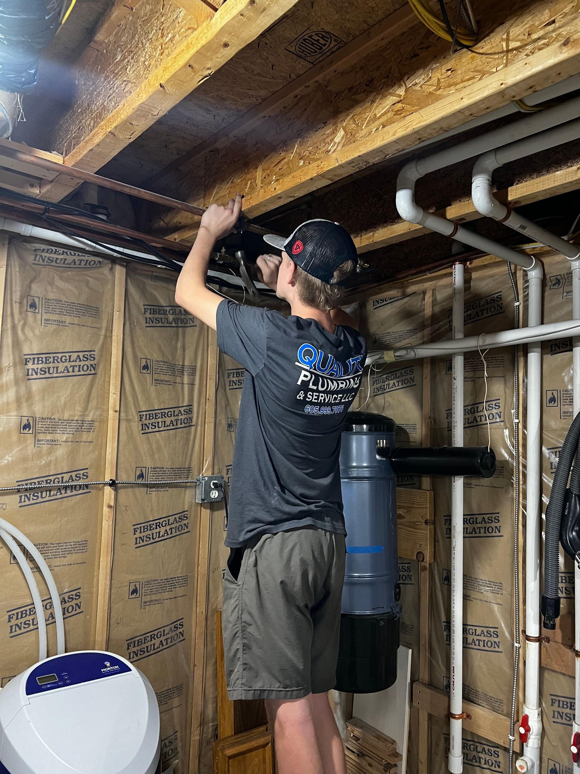 Person works on pipes in a basement, standing near water treatment equipment.