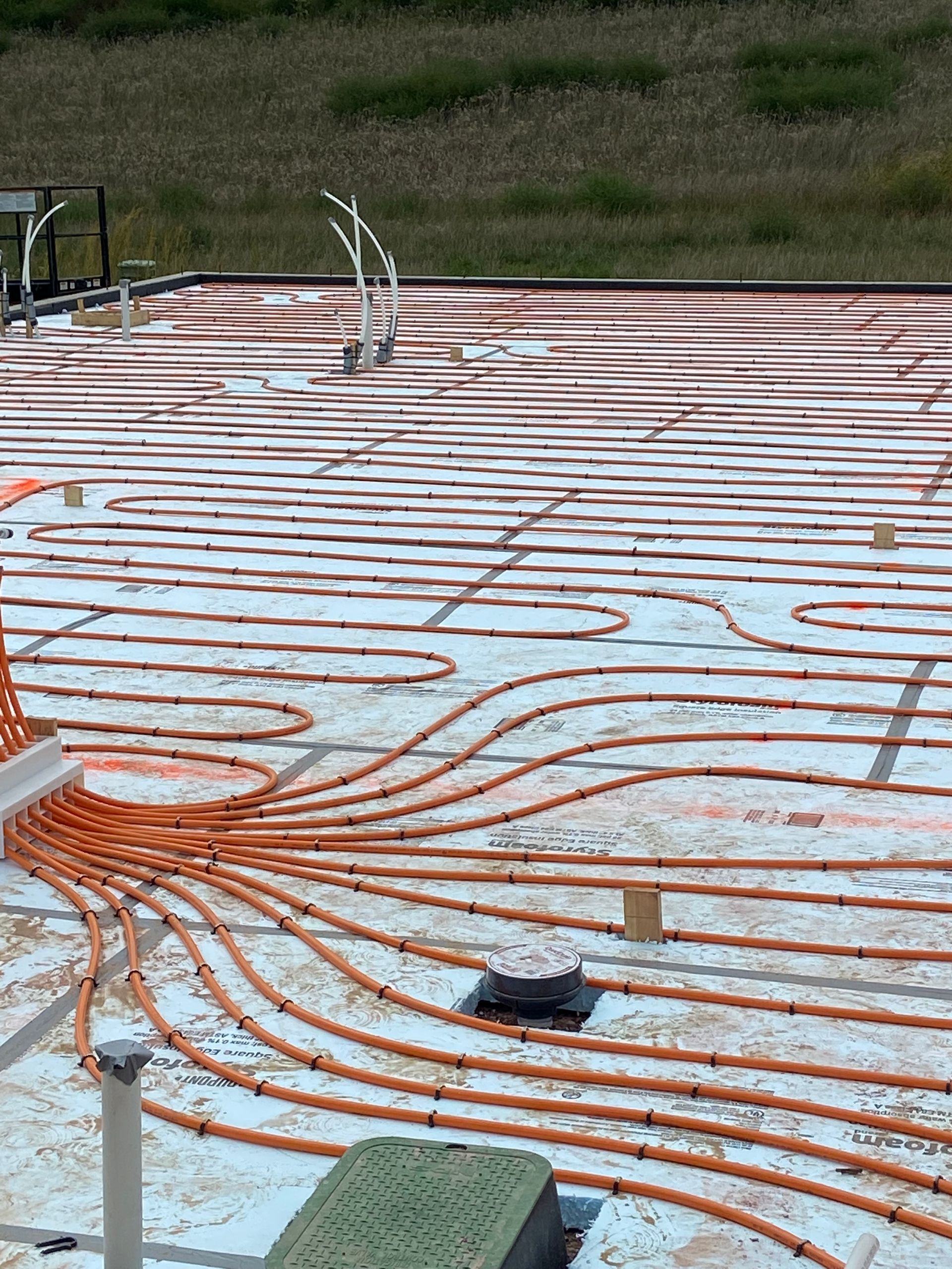 Orange tubing laid on a concrete surface, likely for a radiant floor heating system.