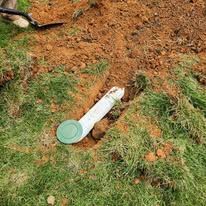 White pipe with green cap in dirt and grass.