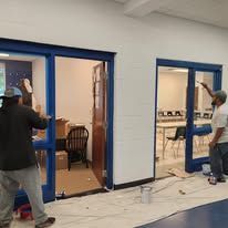 Two people painting a room, one blue door and an interior door are visible.