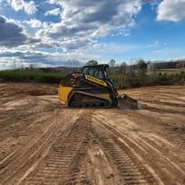 Skid steer loader on a dirt lot under a cloudy blue sky.