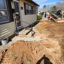 House exterior with dirt, ramp, and a small excavator.