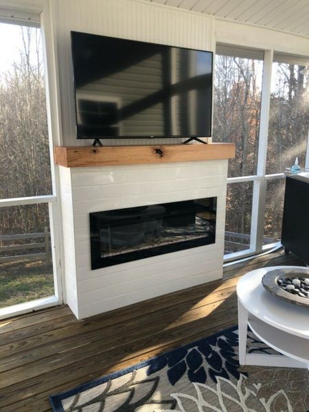 White tiled fireplace with TV and wooden mantle in a screened porch.