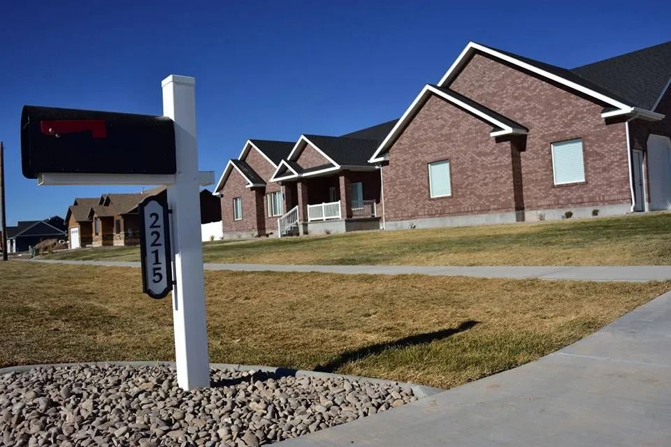 Black mailbox with address plaque in front of brick houses on a grassy hill.