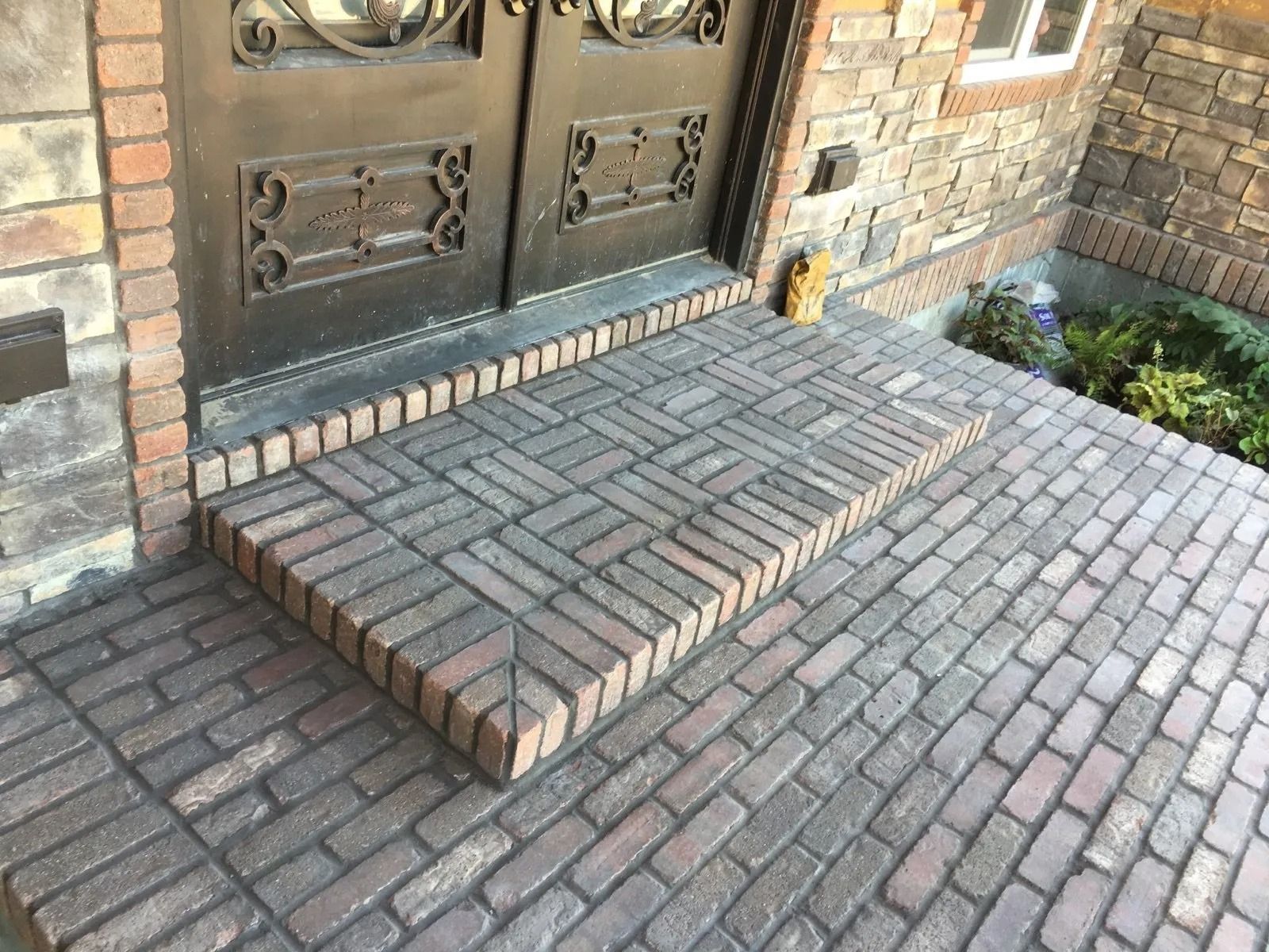 Brick entryway with step leading to ornate iron doors.