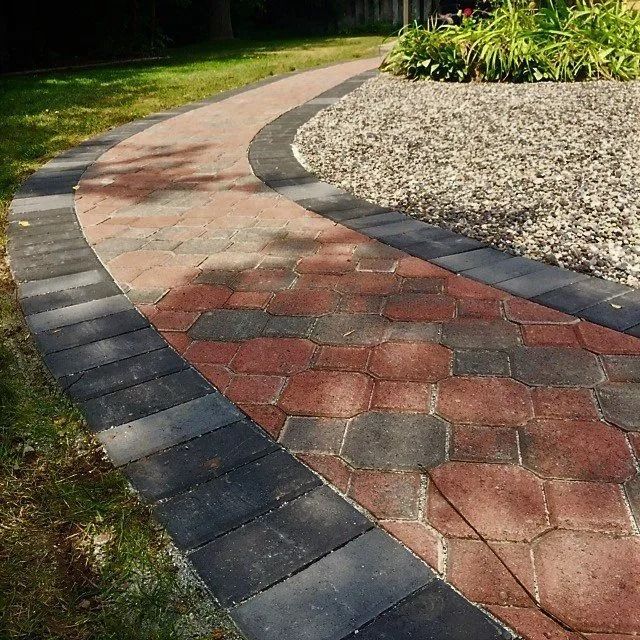 Brick pathway with black borders curving through a grassy lawn, leading to a gravel bed.