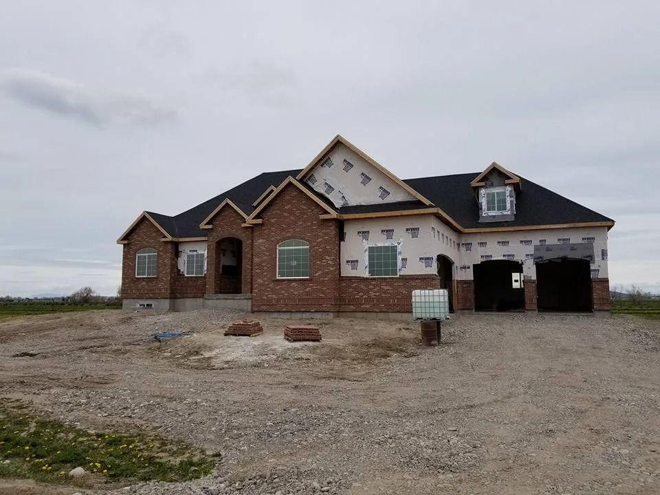 House under construction with brick facade and black roof; gravel lot.