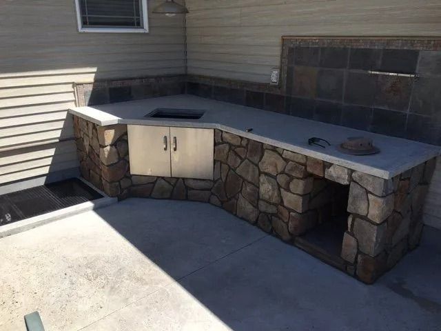 Outdoor kitchen with stone facing and concrete countertop. Includes a grill, storage, and a sink.