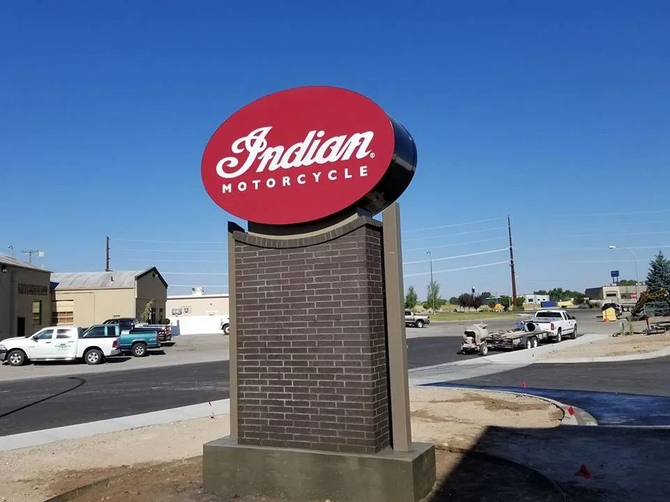 Indian Motorcycle sign with red oval logo atop a brick and gray stone pillar; a sunny day.