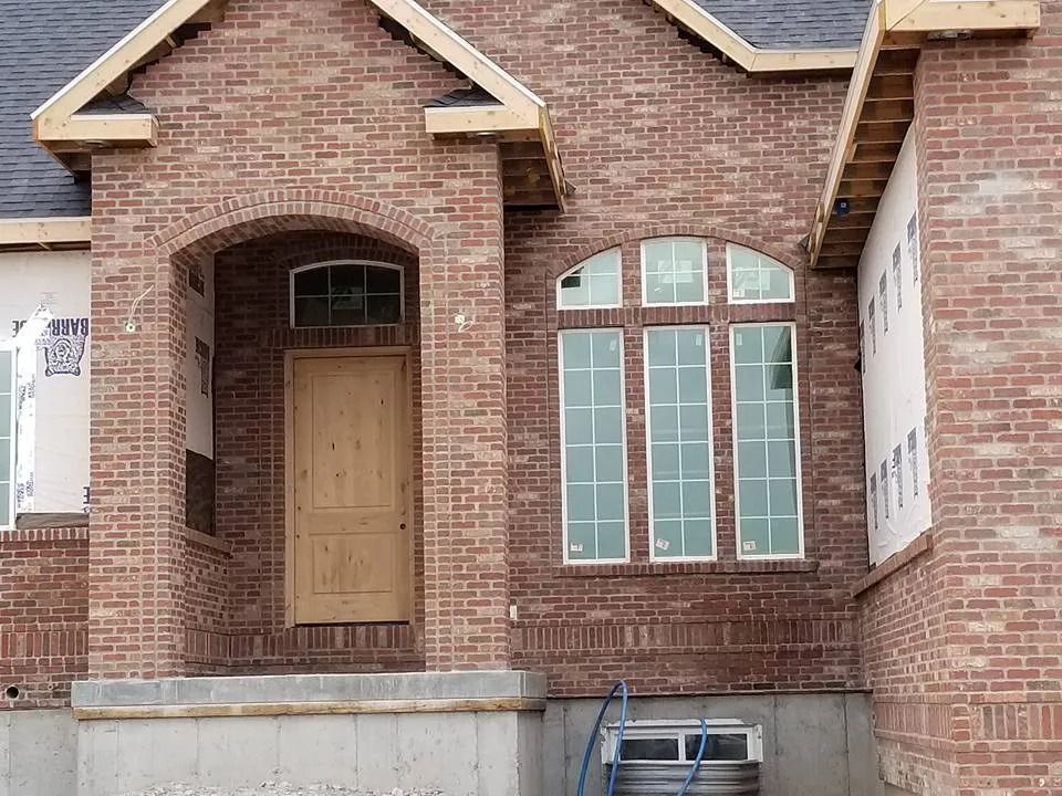 New brick house under construction; arched entry, tall windows, light brown door.