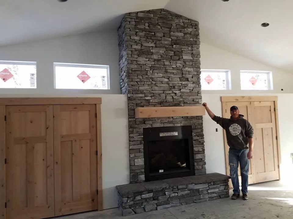 Stone fireplace with wood mantel, flanked by doors and windows, man stands beside it.