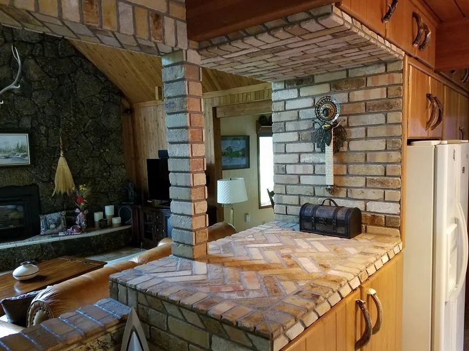 Brick-faced kitchen pass-through with built-in counter and cabinets; living room in background.