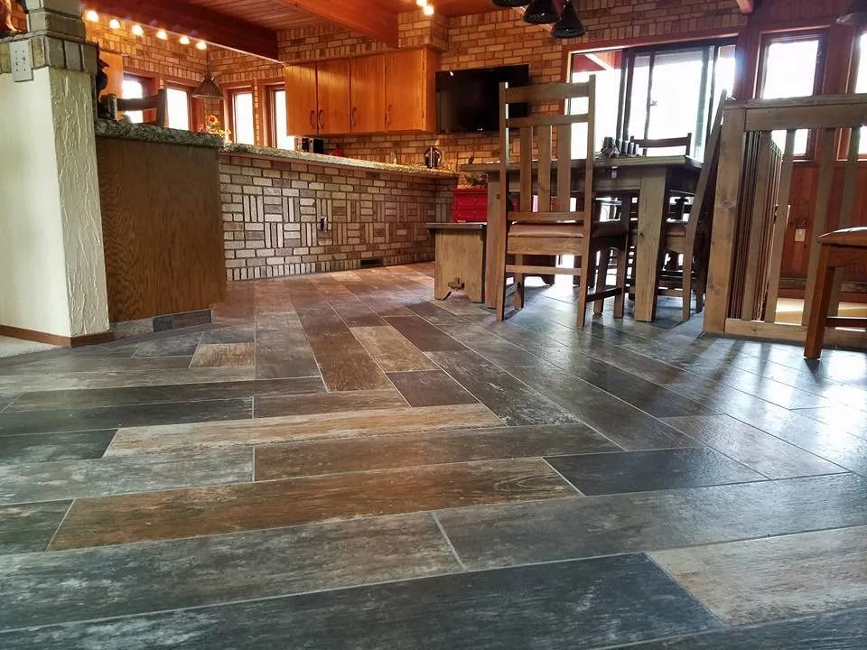 A room with wood-look tile flooring in a herringbone pattern, with a dining table and kitchen bar.
